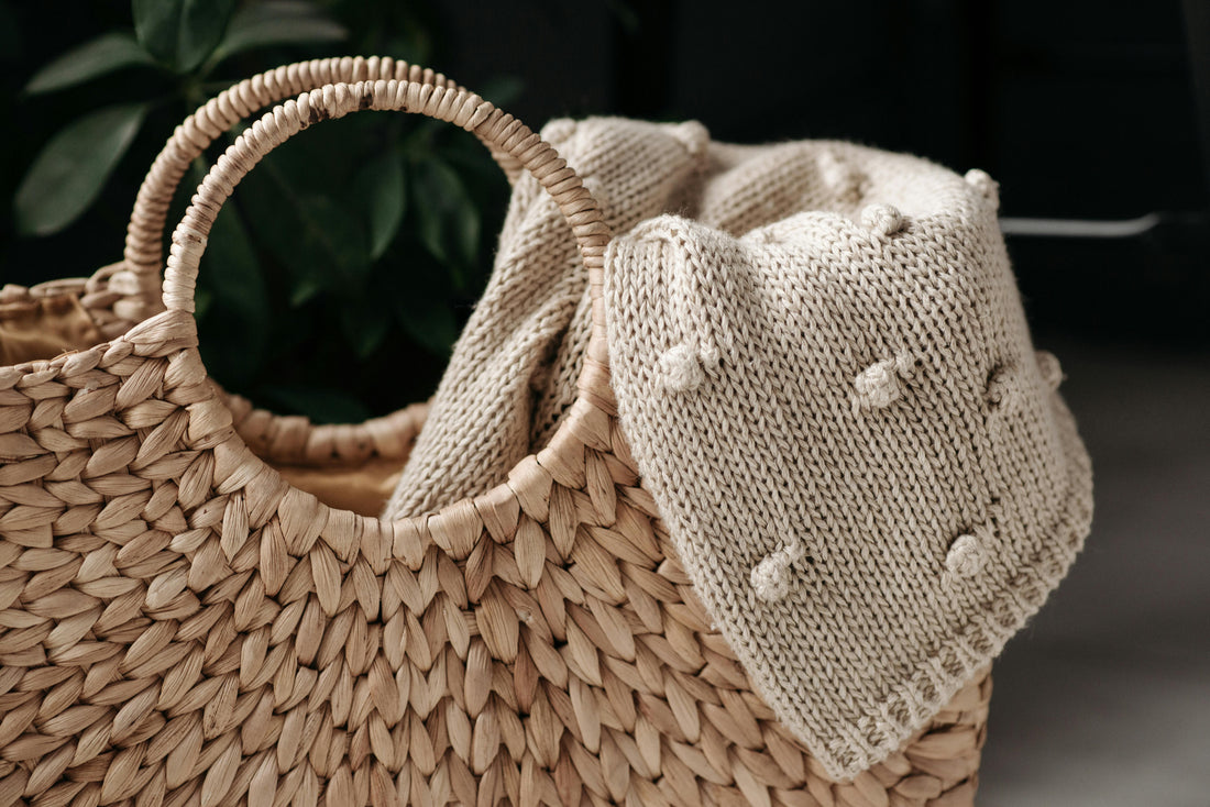 alt="Panier en osier tressé avec poignées rondes, contenant un plaid en maille beige, posé dans un intérieur cosy et naturel"