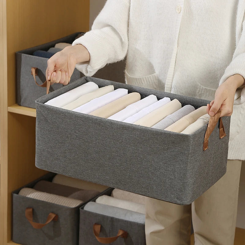 Femme portant un panier de rangement en tissu gris, rempli de vêtements pliés