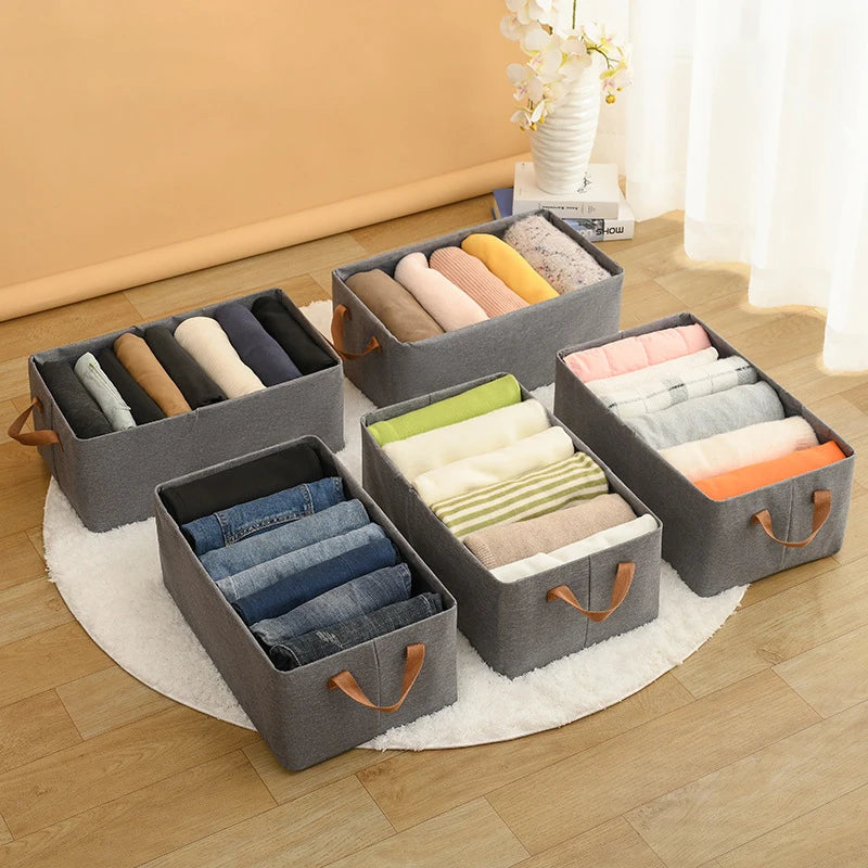 vêtements pliés dans boite de rangement en tissu gris, rectangulaire à poignées, posés au sol