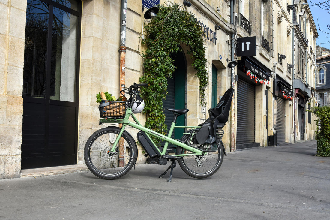 vélo à assistance électrique, sur béquille, sur un trottoir, avec panier avant et siège enfant arrière