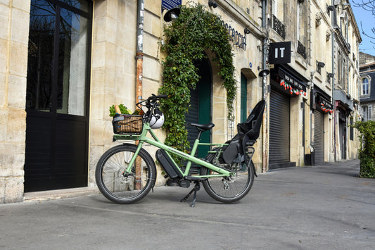 vélo à assistance électrique, sur béquille, sur un trottoir, avec panier avant et siège enfant arrière