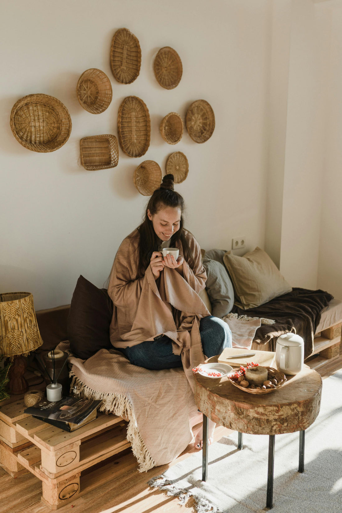 femme assise dans un canapé en palettes, tasse à la main, et paniers accrochés au mur