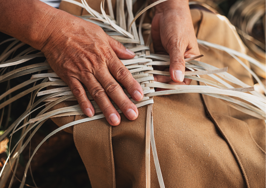 alt="Mains en train de tresser de l'osier pour fabriquer un panier artisanal"