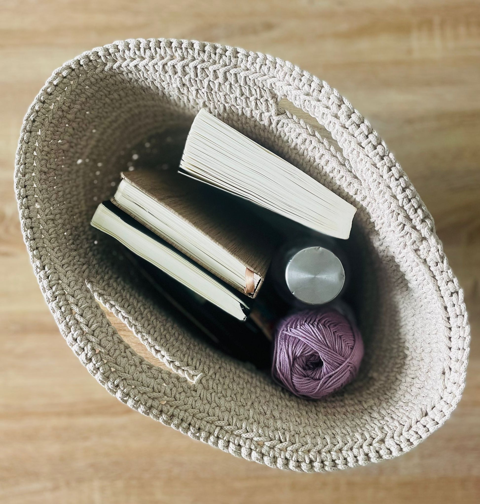 Panier en corde de coton contenant livres, carnet, gourde, pelote de laine

