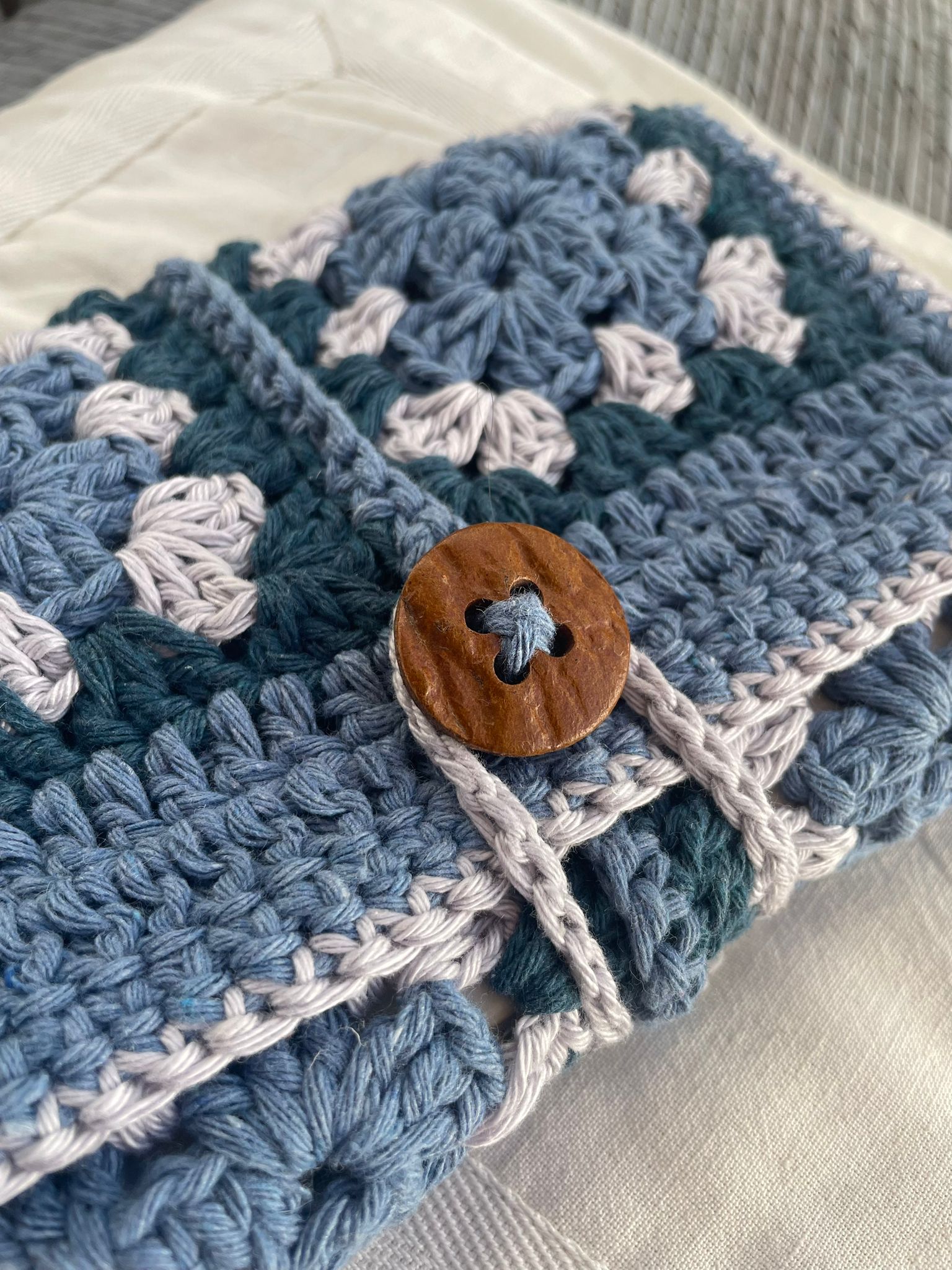 Pochette pour livre, crochetée en coton granny bleu et gris, gros plan sur le bouton en bois
